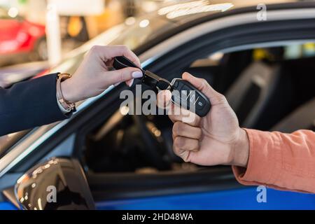 vista parziale del concessionario auto che dà la chiave al cliente africano americano vicino auto sfocata Foto Stock