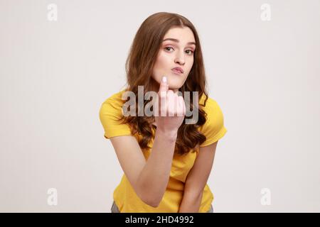 Vieni qui. Ritratto di attraente donna con capelli ondulati di giovane età in abbigliamento casual giallo facendo beckoning gesto, invitando a venire, flirting. Studio interno girato isolato su sfondo grigio. Foto Stock