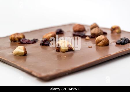 Cioccolato al latte artigianale con nocciole, uvetta e frutta secca su sfondo bianco. Messa a fuoco selettiva Foto Stock