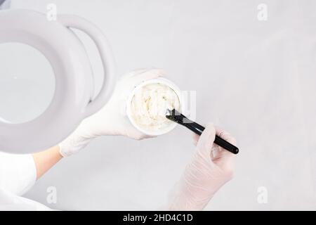 Il cosmetologo prepara una maschera ringiovanente in un bawl per la procedura viso indossando guanti protettivi bianchi. Foto Stock