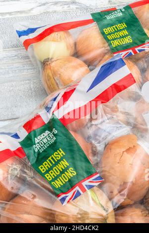 CIPOLLE marroni / Allium cepa confezionate in plastica ASDA. Chiamato anche cipolle gialle. Per gli ingredienti comuni della cucina, Union Jack sul confezionamento alimentare Foto Stock