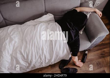 uomo sdraiato su un divano con un mal di testa o un hangover con una bottiglia di birra e una coperta bianca Foto Stock