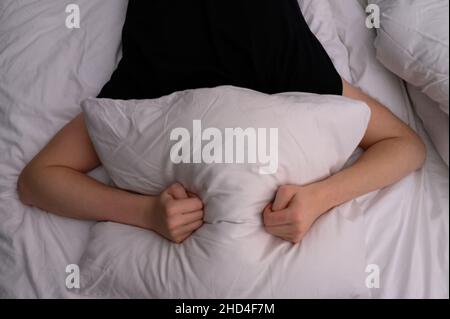 uomo sdraiato a letto e copre la testa con un cuscino. Combatte insonnia, rumore o alzarsi presto la mattina. Foto Stock