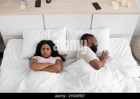 Offese la giovane moglie afroamericana con braccia incrociate sul petto, cant dorme con il marito russante a letto Foto Stock