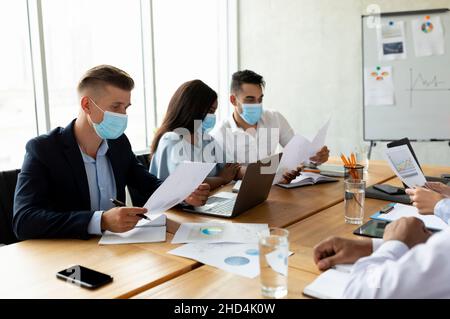 Gruppo di colleghi multietnici che indossano maschere protettive per il viso che lavorano insieme in ufficio Foto Stock