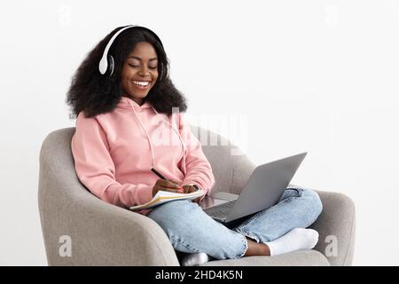 Donna nera positiva che partecipa al webinar, utilizzando notebook e cuffie Foto Stock