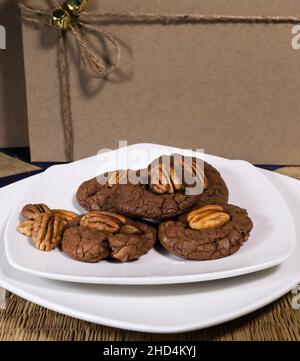 Biscotti al cioccolato con pecan su piatto bianco con confezione regalo riciclata su sfondo Foto Stock