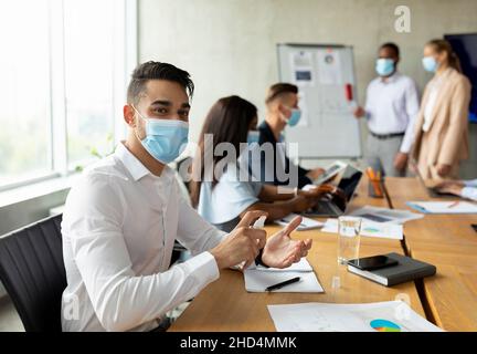 Sicurezza sul luogo di lavoro. Uomo d'affari arabo che indossa la maschera medica utilizzando spray disinfettante in ufficio Foto Stock