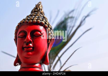 Bella scultura del viso di colore rosso o statua del signore buddha, testa di statua dipinta di colore nero e dorato su piuma di pavone con cielo sul backgro Foto Stock