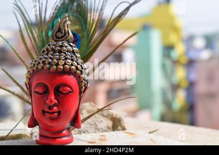 Bella scultura del viso di colore rosso o statua del signore buddha, testa di statua dipinta di colore nero e dorato su piuma di pavone con cielo sul backgro Foto Stock