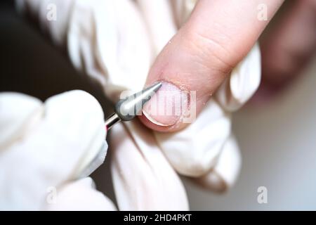 Donna nel salone delle unghie che riceve manicure nel salone di bellezza da estetista che usano il trapano elettrico della lima delle unghie con la polvere di volo di scoppio e detriti intorno. Concetto di cura delle unghie. Foto Stock