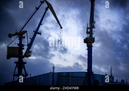 Wismar, Germania. 03rd Jan 2022. Le nuvole scure si riuniscono di sera sul sito MV Werften con gru, un'ex nave residenziale per i lavoratori dei cantieri navali e la grande sala di costruzione navale. Per il momento, lo stato di Meclemburgo-Pomerania anteriore non deve versare un prestito di aiuto concordato di 78 milioni di euro (88 milioni di dollari USA) al proprietario di MV Werften Genting Hong Kong. La crisi a MV Werften, che attualmente conta circa 2.000 dipendenti e attività a Stralsund, Rostock e Wismar, continua a venire in testa. Credit: Jens Büttner/dpa-Zentralbild/dpa/Alamy Live News Foto Stock