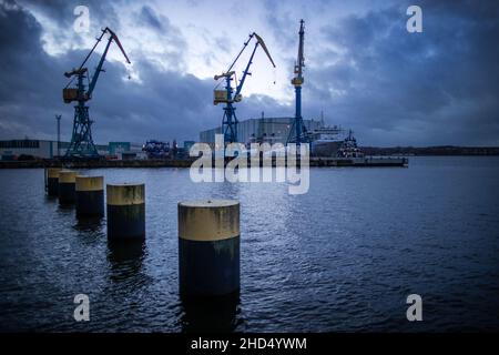 Wismar, Germania. 03rd Jan 2022. Le nuvole scure si riuniscono di sera sul sito MV Werften con gru, un'ex nave residenziale per i lavoratori dei cantieri navali e la grande sala di costruzione navale. Per il momento, lo stato di Meclemburgo-Pomerania anteriore non deve versare un prestito di aiuto concordato di 78 milioni di euro (88 milioni di dollari USA) al proprietario di MV Werften Genting Hong Kong. La crisi a MV Werften, che attualmente conta circa 2.000 dipendenti e attività a Stralsund, Rostock e Wismar, continua a venire in testa. Credit: Jens Büttner/dpa-Zentralbild/dpa/Alamy Live News Foto Stock