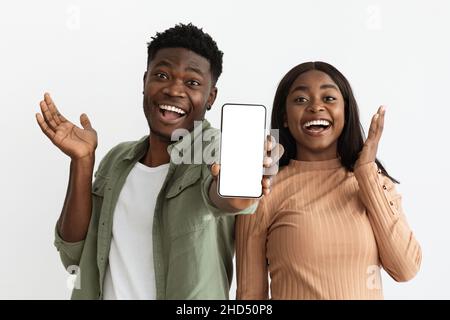 Emozionale coppia afroamericana che mostra smartphone con schermo vuoto, mockup Foto Stock