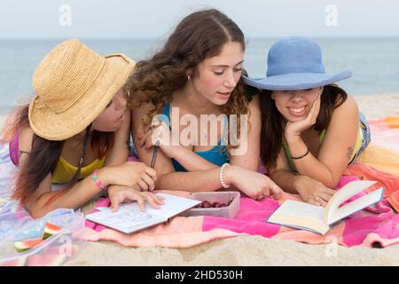 Tre fidanzate di età universitaria condividono un libro sulla spiaggia Foto Stock