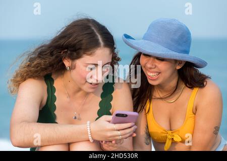 Due giovani donne in spiaggia che guardano il cellulare. Foto Stock