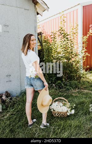 La donna sorridente tiene un grande cappello e ha fiori in tasca posteriore Foto Stock