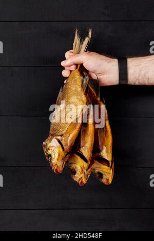 Mano maschile che tiene tre birre affumicate sul nero Foto Stock