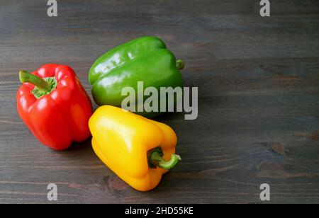 Vibrant Tricolor Bell Peppers allineato su sfondo di legno posteriore Foto Stock