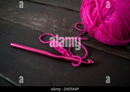 palla di lana rosa ravvicinato con uncinetto rosa su terreno di legno fatto a mano Foto Stock