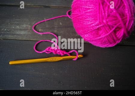 palla di lana rosa da vicino con uncinetto giallo su terreno di legno fatto a mano Foto Stock