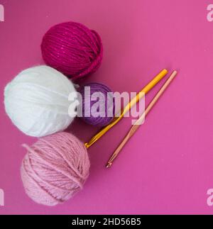 palline di lana colorate su terreno rosa con uncinetto ganci fatti a mano Foto Stock
