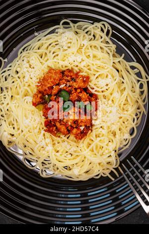 Spaghetti bolognese tradizionali. Composizione alimentare con pasta calda in un piatto nero con forchetta. Mediterraneo, cucina italiana, piatto semplice. Disposizione piatta, chiusura Foto Stock
