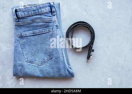 Jeans classici da donna blu con cintura su sfondo grigio di cemento. Tessuto in denim. Abbigliamento casual. Vista dall'alto. Comodo panno stile. Disposizione piatta Foto Stock