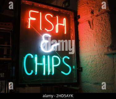 I pesci e le patatine al neon firmano in tubo al neon rosso e verde su una parete di pietra racchiusa in una scatola di vetro e legno Foto Stock