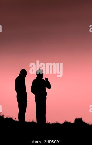 Due persone in piedi sul sentiero costiero si sono squarciate contro un cielo colorato alla fine della giornata a Newquay in Cornovaglia. Foto Stock