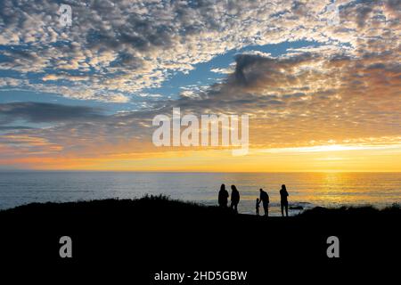 I turisti che si erono sulla costa silhouette da uno splendido e colorato tramonto su Little Fistral sulla costa di Newquay in Cornovaglia. Foto Stock