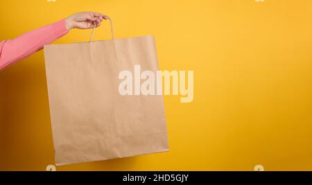 donna che tiene in mano marrone bianco sacchetto di carta del mestiere per il takeaway su sfondo giallo. Modello di imballaggio. Concetto di servizio di consegna, banner Foto Stock