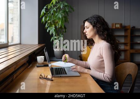 Giovane dipendente femminile che lavora su un computer portatile e che fa esercizi manuali per prevenire la sindrome del tunnel carpale Foto Stock