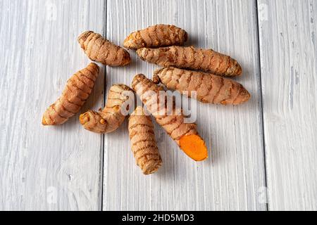 Radici fresche intere di curcuma su un tavolo di legno bianco. Primo piano rizomi di curcuma cruda organica. La curcuma longa è un ingrediente in polvere di spezie e curry. Foto Stock