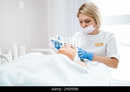 Medico femminile con scrubber ultrasonico che fa la procedura di ecografia pulizia del viso della donna. Peeling professionale della pelle del viso Foto Stock