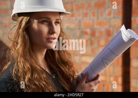 Lavoratrice di costruzione femminile in elmetto che regge i progetti Foto Stock