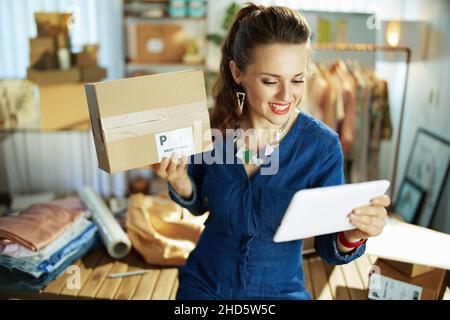 Felice elegante 40 anni piccola impresa proprietario donna con pacco avendo webcam riunione su un tablet PC in ufficio. Foto Stock