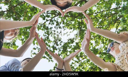 Un gruppo di ragazze fa una forma del cuore dalle loro mani contro lo sfondo dei rami dell'albero. Foto Stock