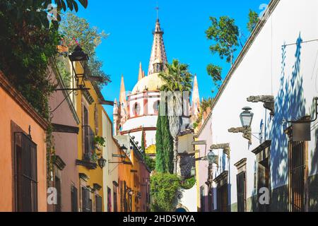 Lanterne ornamentali e disegni unici per i canales tra case colorate su Aldama Street con vista della cupola per la Parroquia in SMA, Messico Foto Stock