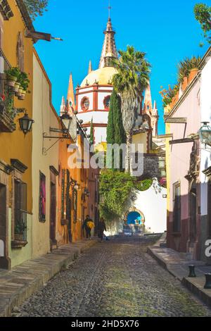 Stretta Cobblestone Aldama strada offre Vew della Parroquia San Miguel de Allende Arcangel Chiesa Dome accanto a case colorate in SMA, Messico Foto Stock