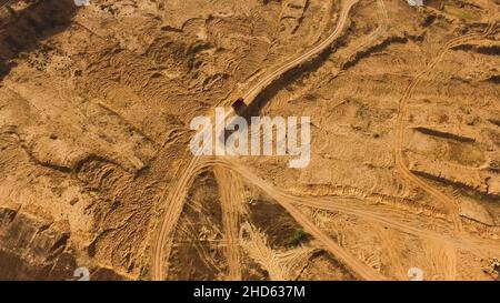 Vista dall'alto della strada in sabbia polverosa con cingoli ruote e carrello rosso di guida. Camion in movimento e lasciando un percorso polveroso in aria, ruote pesanti, macchinari Foto Stock