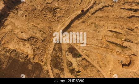 Vista dall'alto della strada in sabbia polverosa con cingoli ruote e carrello rosso di guida. Camion in movimento e lasciando un percorso polveroso in aria, ruote pesanti, macchinari Foto Stock