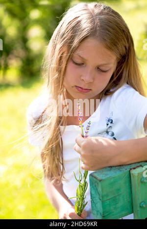 la ragazza pensiva siede su una panca con un bouquet di fiori vicino ad una casa privata Foto Stock