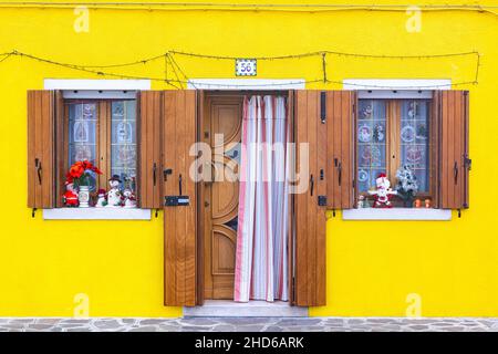 Primo piano simmetrico di una facciata in gesso giallo dai colori vivaci con finestre con vasi di fiori e una porta Foto Stock