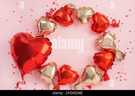 Un grande rosso e molti piccoli palloni d'aria di forma a cuore su sfondo rosa festivo. Concetto di amore. Festa. San Valentino o matrimonio Foto Stock