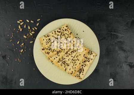 biscotti croccanti a grani interi su un piatto bianco con semi di sesamo e lino. primo piano. sfondo nero Foto Stock
