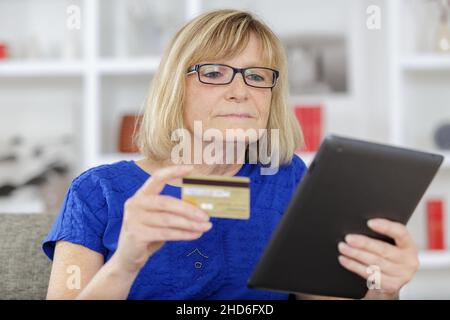 donna anziana che dà la carta di credito sul tablet Foto Stock