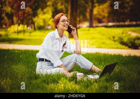 Giovane studentessa lavora con il computer portatile, all'aperto mentre si siede sull'erba. Istruzione. Comunica Foto Stock