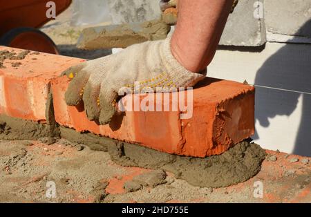 Costruzione in muratura. Un muratore sta posando mattoni su mortaio usando una cazzuola, una linea di corda, o una linea di livello per costruire una superficie orizzontale del bric Foto Stock
