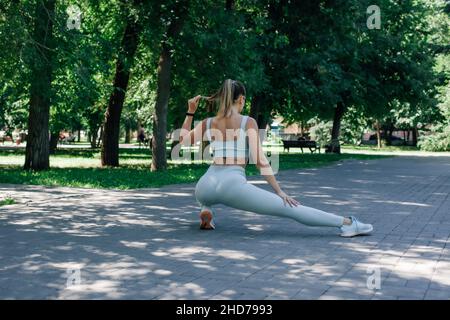 ritratto di giovane donna sportiva che fa yoga, si scalda, si allunga in grigio sportswear nel parco nella soleggiata giornata estiva Foto Stock